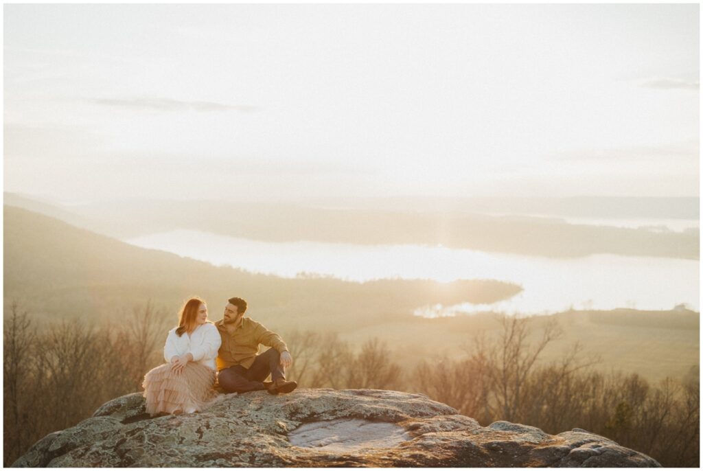 couple sit on edge of cliff overlooking lake