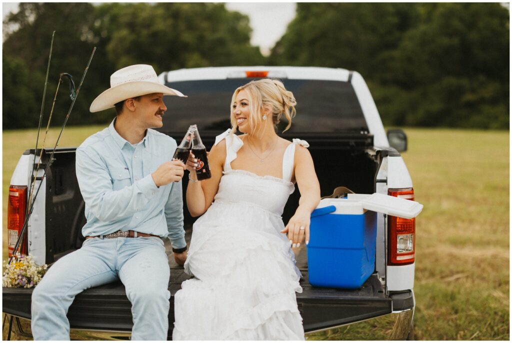 couple sitting in on back of pickup truck sipping a bottle of soda